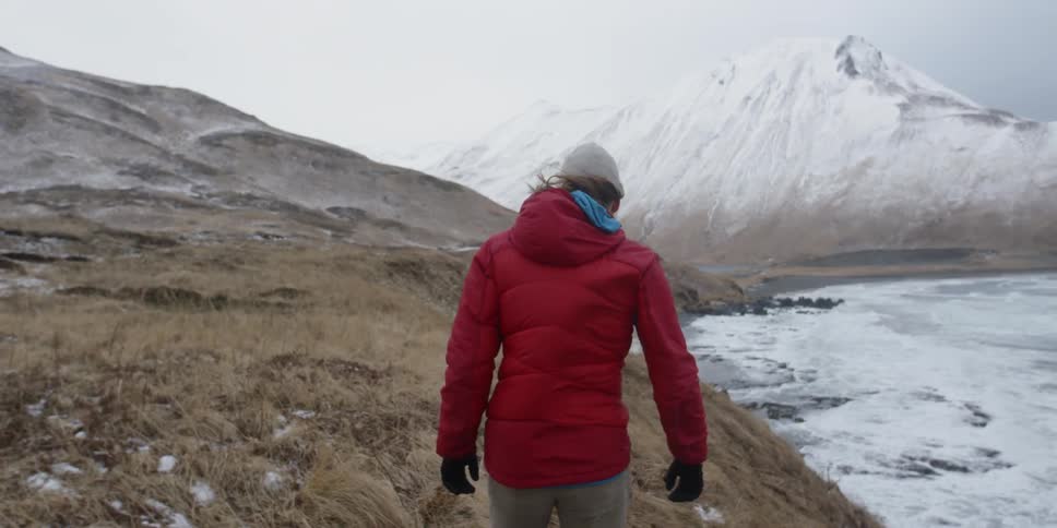 A person walks along a cliff near an icy beach