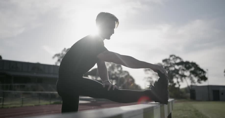 A man stretches on the railing of a running track