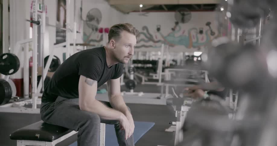 A man sits on a weight bench in a gym