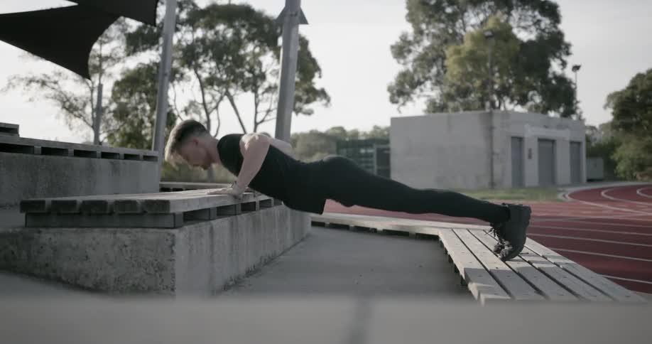 A man does push-ups on outdoor bleachers