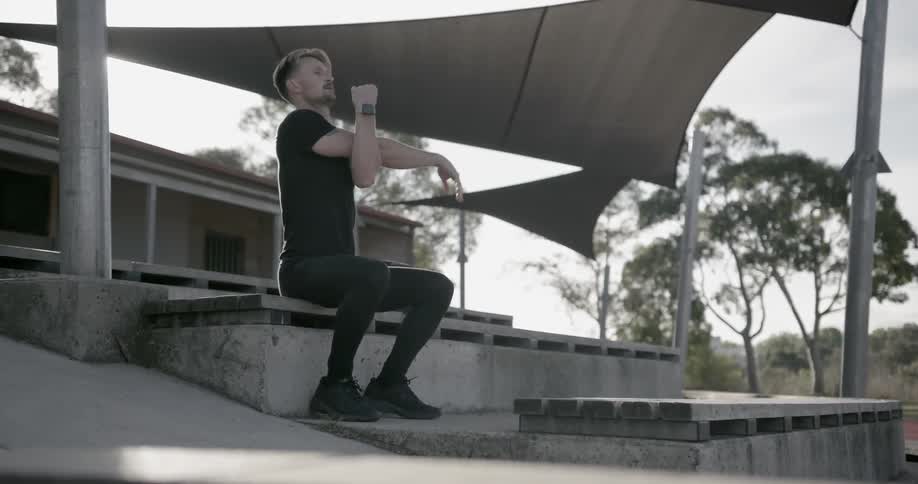 A man sits on outdoor bleachers while stretching his arms
