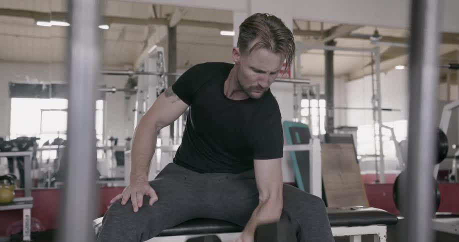 A man is doing arm curls with a weight in a gym during the day