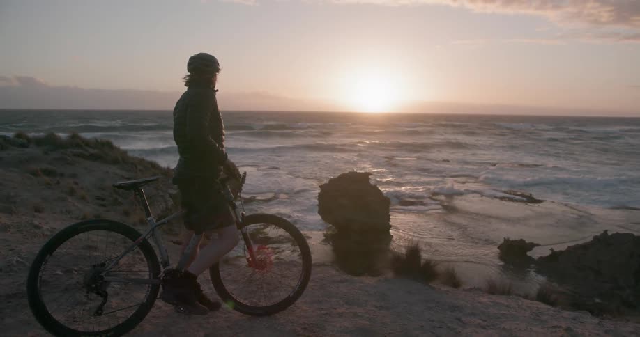 A bicyclists is taking in a coastal view at sunset