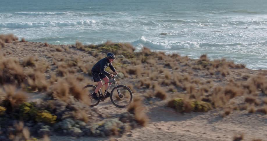Man rides a bike through a path lined with clumps of grass