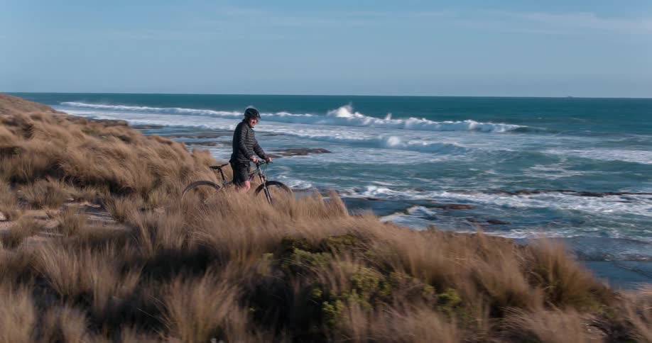 A bicyclist sits atop a cliff by the shore