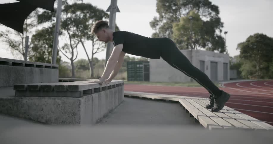 A man does push-ups on outdoor bleachers