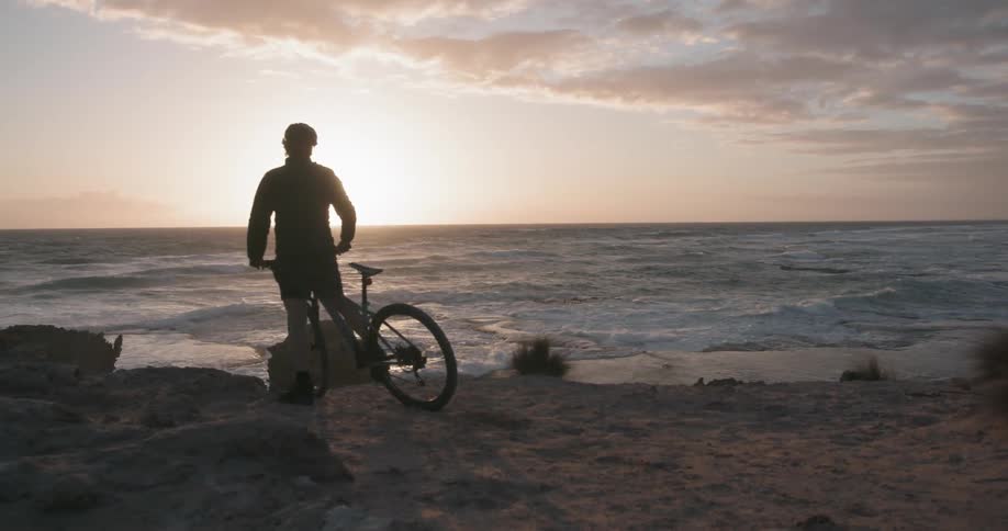 A man rides his bike to an oceanside ledge