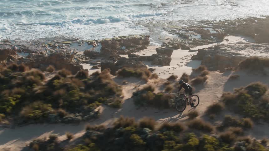 A man rides his bike on the small sandy trail