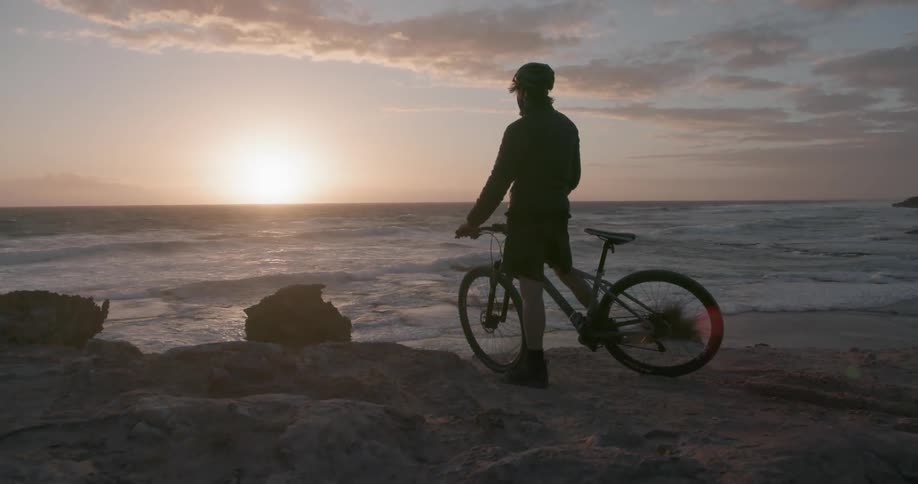 A man on a bicycle sits and looks out onto the water