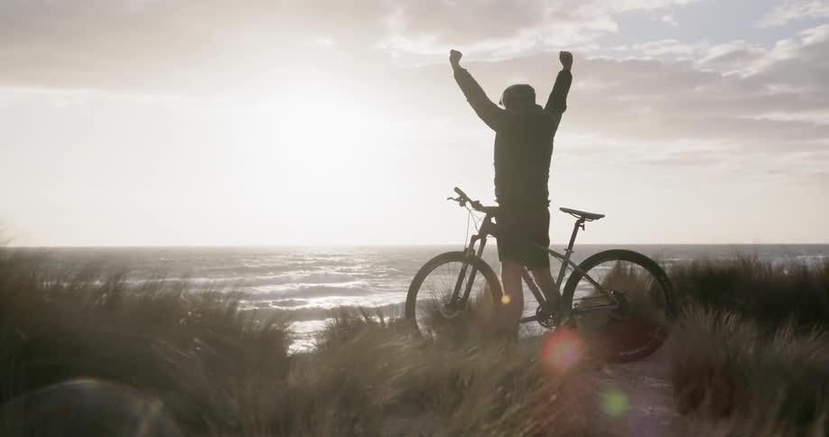 A man cheers on a bike near the ocean