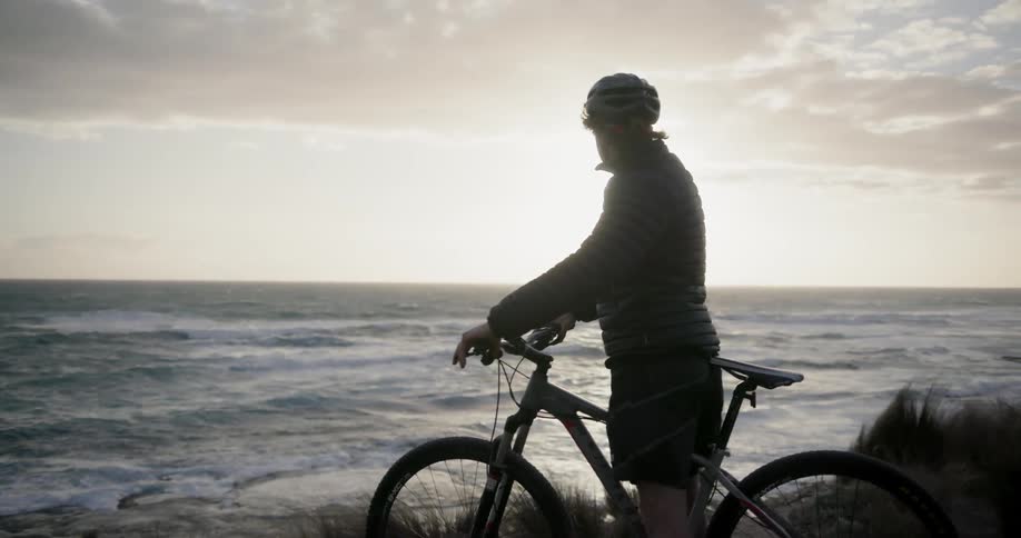 A bicyclist stops to watch a coastal sunset
