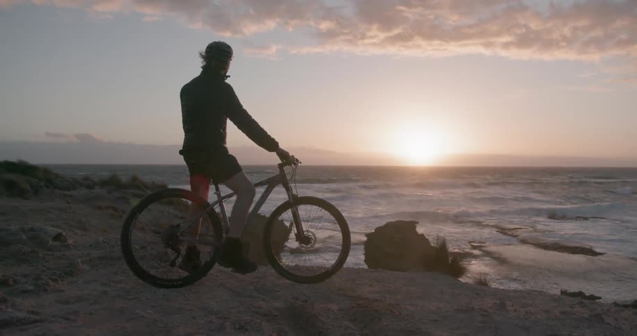 A bicyclists is taking in a coastal view at sunset