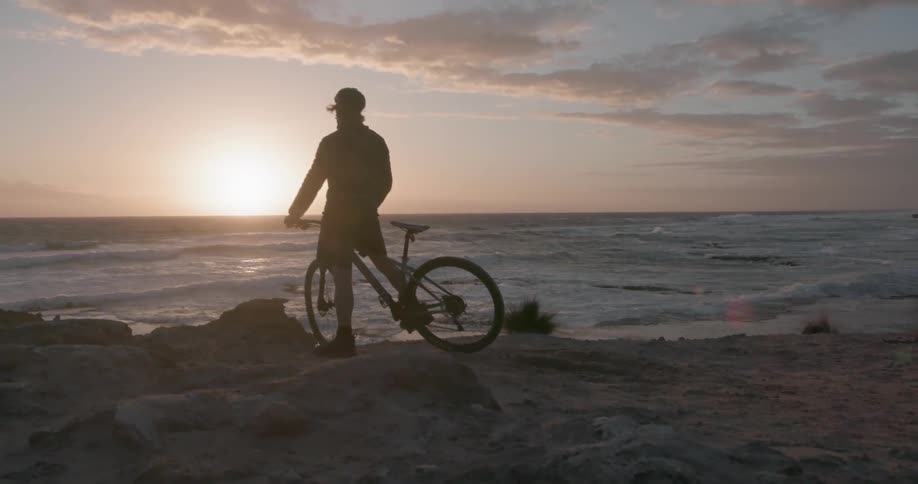 A bicyclist stops to look at a sunset on the coast