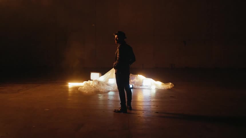 Man stands next to televisions covered with a sheet in a warehouse