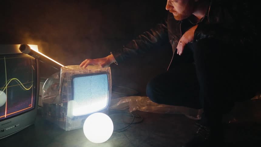 Man crouches next to tvs on the floor of a smoky room