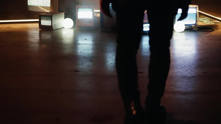 Man walks towards tvs on the floor of a dark room
