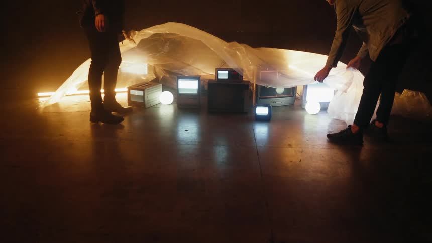 Two men put a plastic sheet over tvs on the ground