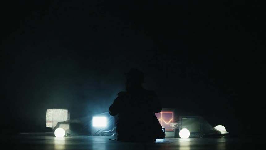 Man sits next to tvs on the floor in a dark room