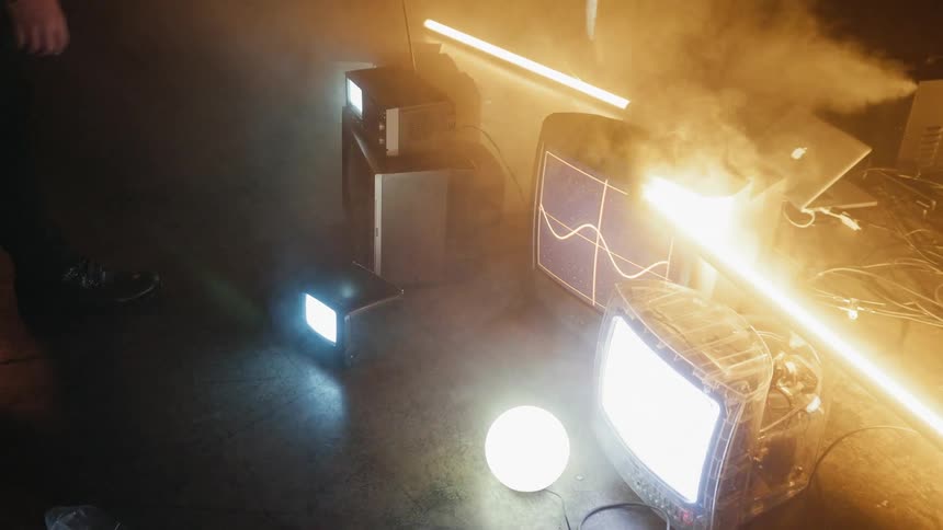 A man crouches next to tvs on the floor of a smoky room