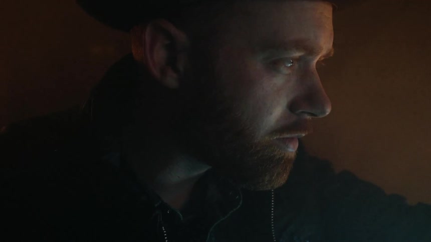 A man is standing in the dark as light flickers on his face