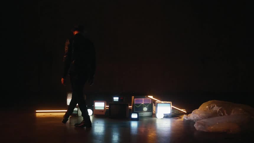 Man stands next to tvs on the floor of a dark room