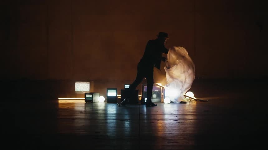 A man is pulling a plastic sheet of a collection of monitors on the floor in a dark room
