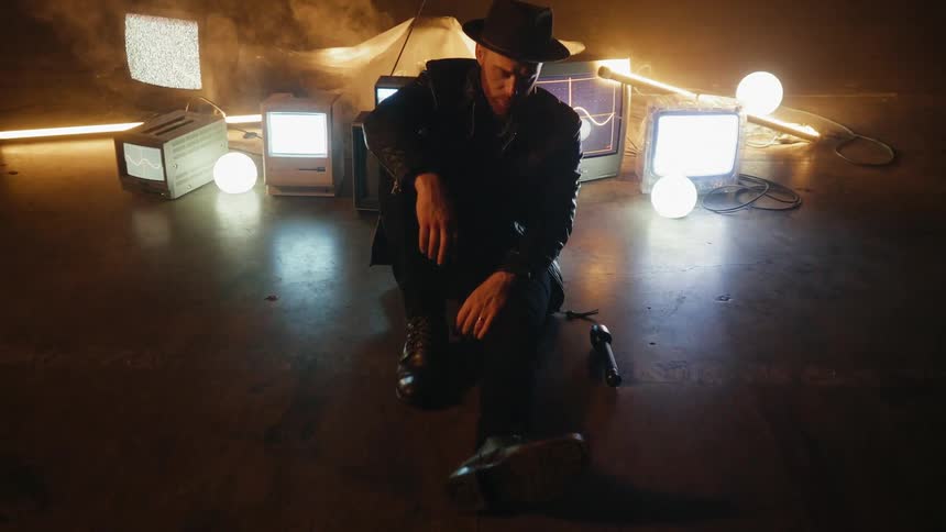 A man sits next to tvs on the floor of a smoky room