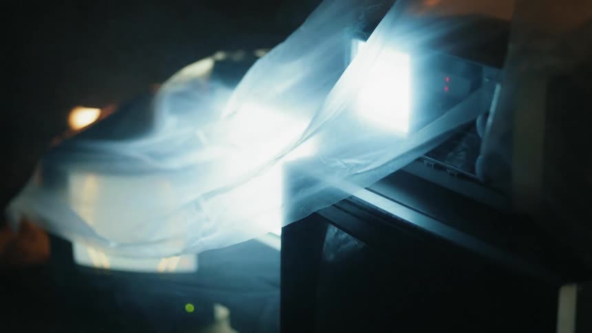 Tvs glow beneath a plastic sheet in a dark room