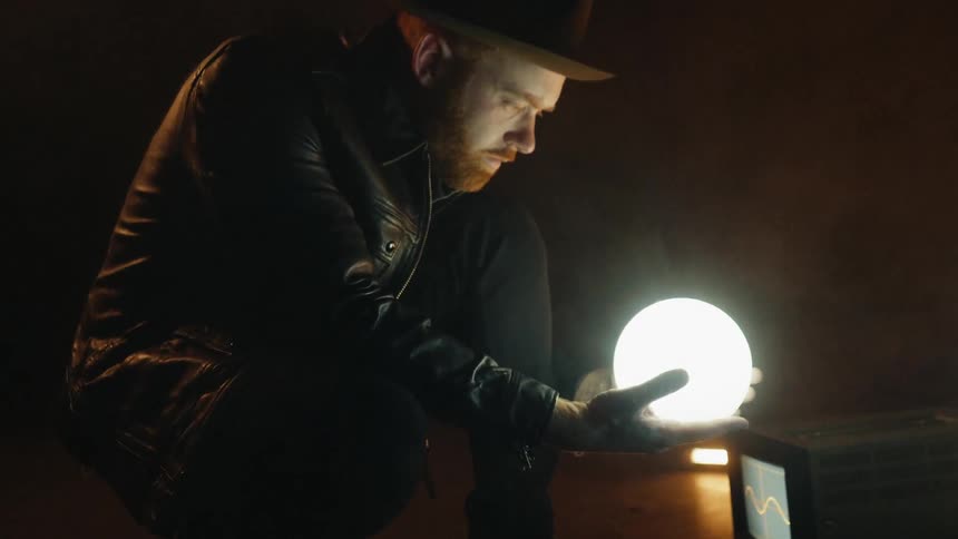 Man lifts a glowing sphere while crouching in a dark room