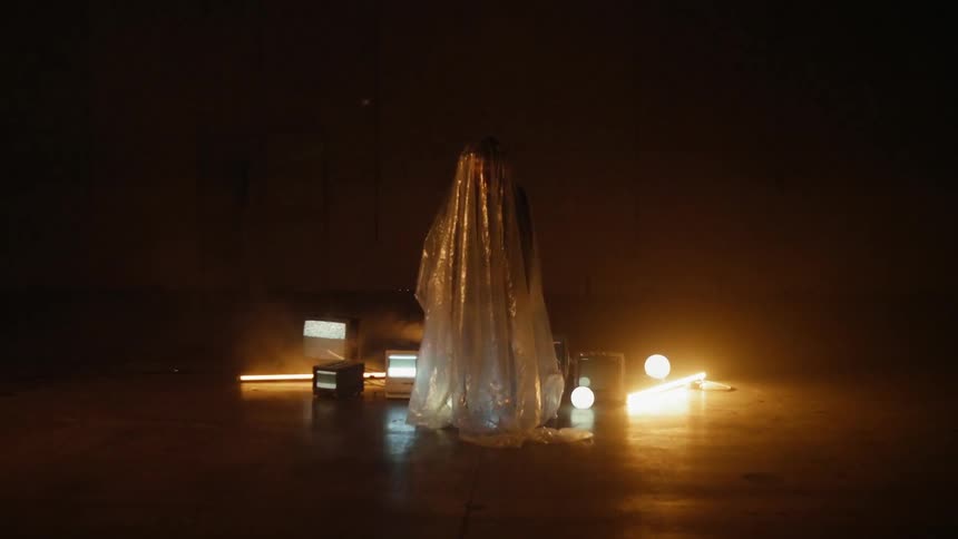A man is standing beneath a plastic sheet in a room with monitors