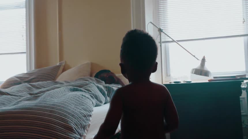 Boy running down a hallway and then approaches a bed that someone is sleeping in