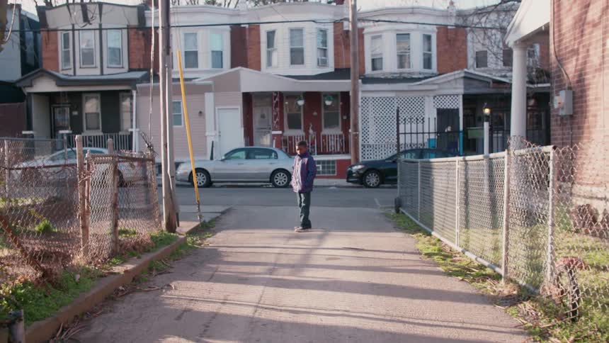 A boy is standing with his hands in his pockets at the end of a driveway during the day