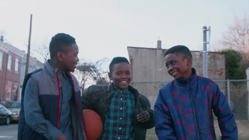 Three smiling boys walk down the street congratulating each other