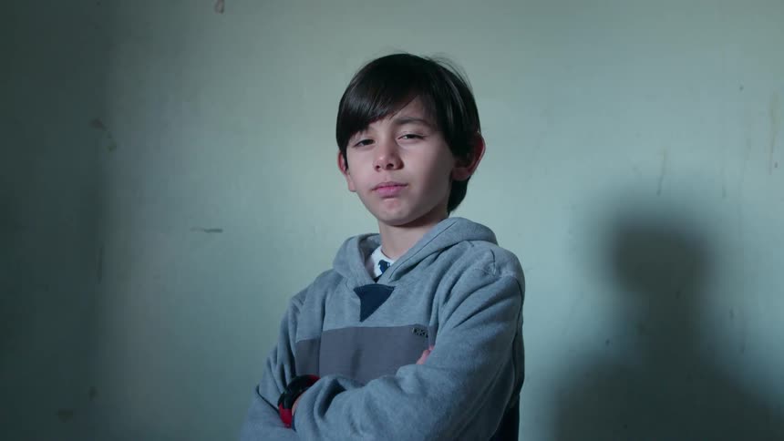 A young boy with his arms crossed squints his eyes