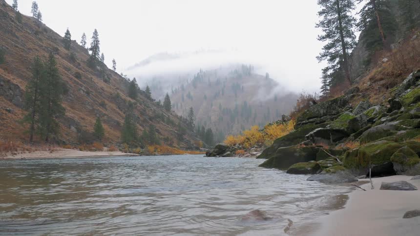 The water is rough splashing against the shore by the hills