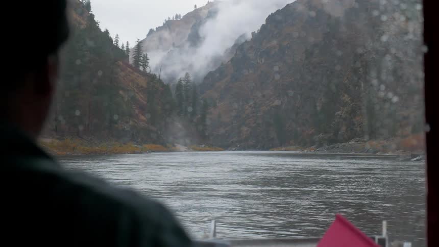 A man is navigating boat on a waterway in a mountainous area on a stormy day