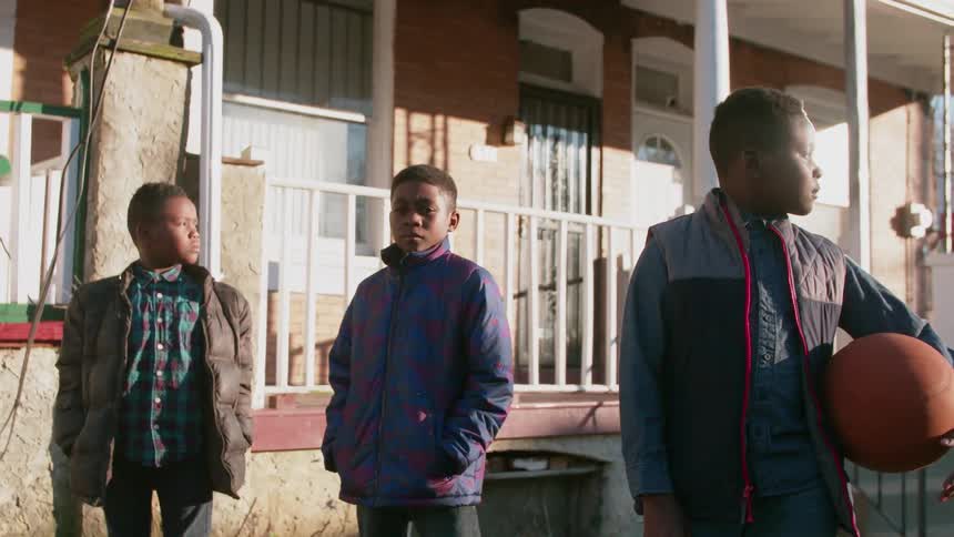 Three boys are standing outside a home during the day