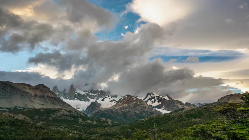Clouds pass over snow capped mountains and green hills