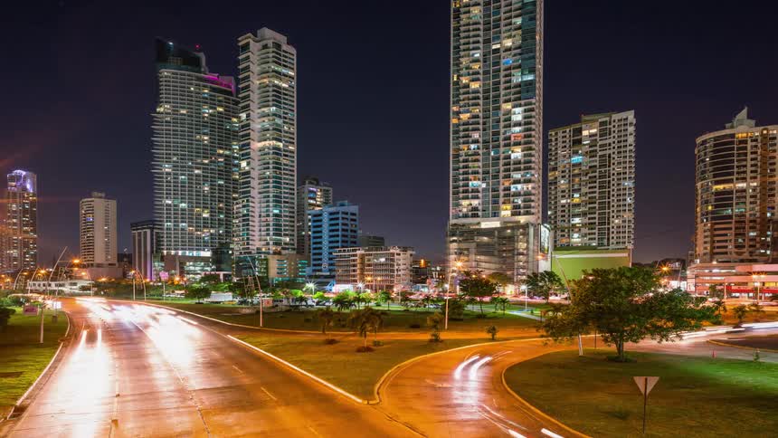 The cars speed around the road by the city at night