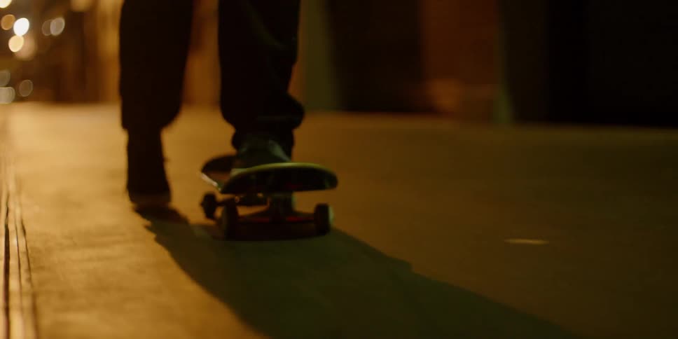 A skateboarder is riding on a city sidewalk at night
