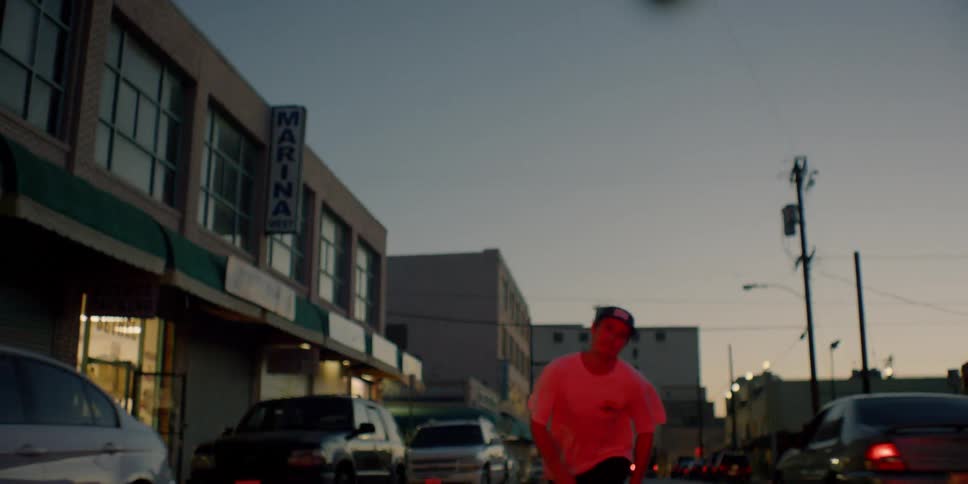 A teenager is riding a skateboard on a city street at dusk