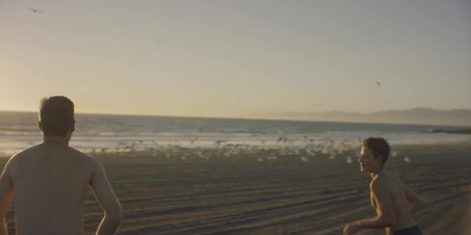 Two boys run towards the ocean on the beach