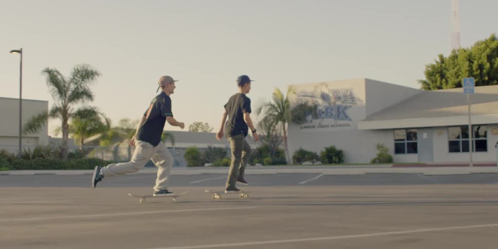 Two men ride their skateboards in the parking lot