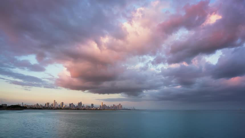Clouds are moving across the sky over a city on the coast at dusk