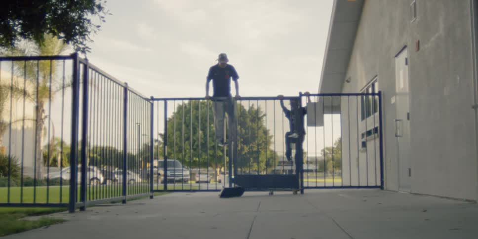 Two men with skateboards climb the fence