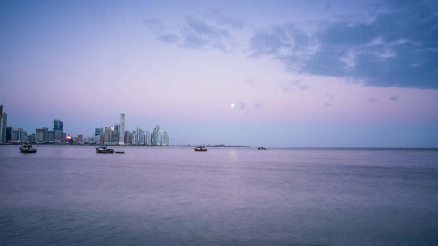 Boats drift in the bay near a city at dawn