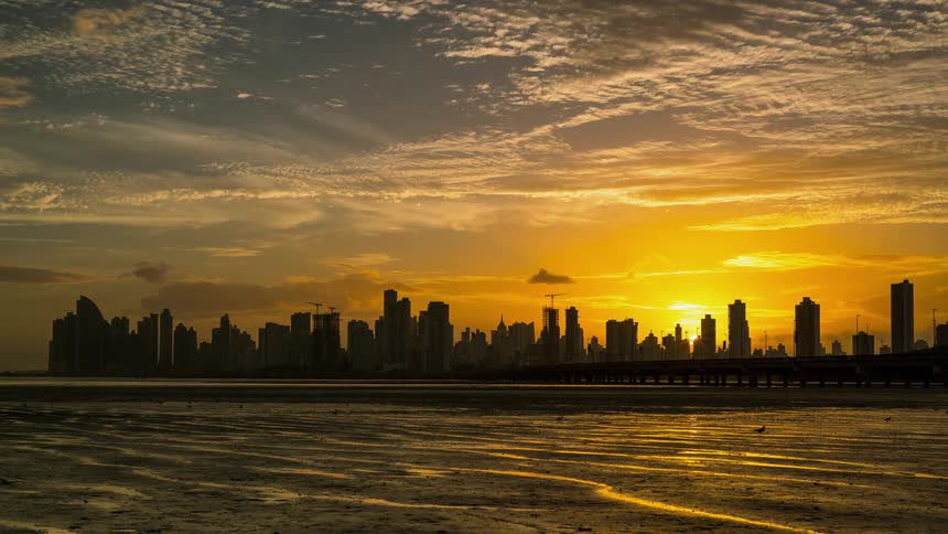 Clouds are drifting over a coastal city and bay as the sun sets