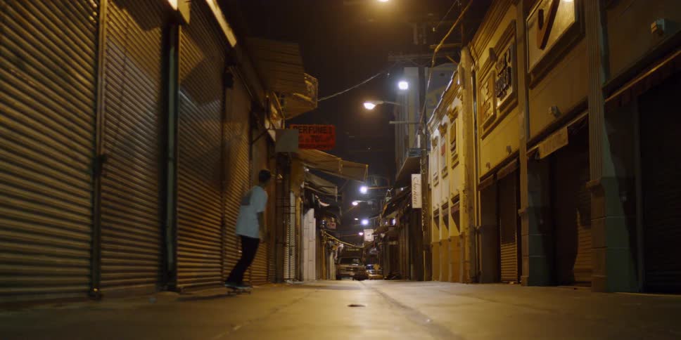 A man is riding his skateboard down the dark alley
