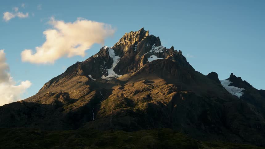 Clouds are drifting across a mountain peak during the day