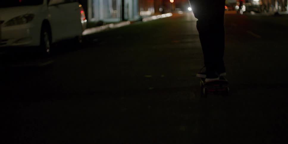 A man rides his skateboard on a windy night